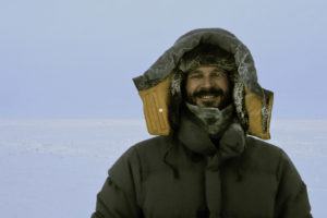 Board member Aaron Cooke, smiling and wearing several large, fur lined coats