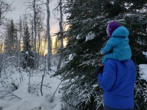 Parent with child on shoulders walking in snowy forest